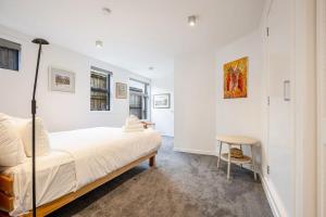 a white bedroom with a bed and a stool at Stylish and serene living in Kohimarama in Auckland