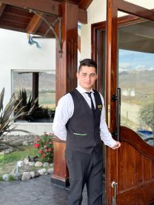 un hombre con chaleco y corbata parado en una puerta en Edenia Hotel & Nature en El Calafate