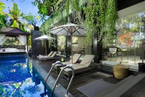 a pool with chairs and an umbrella next to a house at Villa Balimu Seminyak in Seminyak