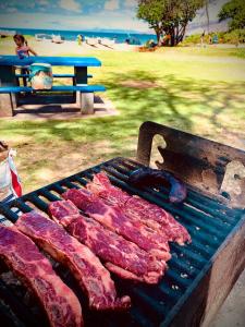 a grill with meat on it with a beach in the background at Embark on a journey through Maui with Aloha Glamp's jeep and rooftop tent allows you to discover diverse campgrounds, unveiling the island's beauty from unique perspectives each day in Haiku