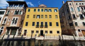 un edificio giallo seduto accanto a un fiume di Ca' Messner 5 Leoni a Venezia