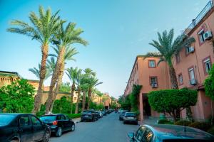 Riad The Moroccans Pool And Terrace في مراكش: شارع تصطف فيه أشجار النخيل والسيارات المركونه