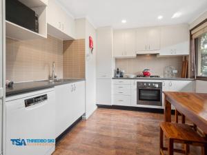 a kitchen with white cabinets and a wooden table at Chamonix in Thredbo