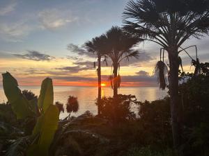 um pôr do sol na praia com palmeiras e o oceano em Fumiko Rina Acop em San Juan
