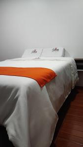 ein weißes Bett mit orangefarbenem Kissen darauf in der Unterkunft GOLDEN PARIS Hotel in Ayacucho