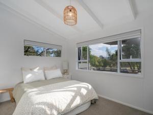 a white bedroom with a bed and two windows at Sol Vista Paku - Pauanui Holiday Home in Pauanui