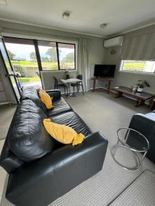 a living room with a black leather couch with yellow pillows at Coastal Golf & Spa Guesthouse in Mount Maunganui