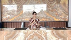 Una donna in piedi dietro un bancone con le braccia incrociate di The Malioboro Hotel & Conference Center a Yogyakarta