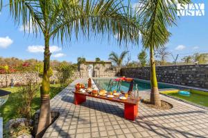 a table with fruit on it sitting under two palm trees at Corbett Calling with Jacuzzi & Projector Set-Up by StayVista in Rāmnagar