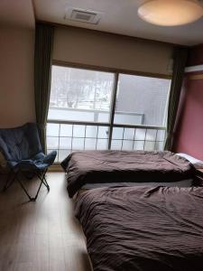 a bedroom with two beds and a chair and a window at フューディズコンドミニアム定山渓 in Jozankei