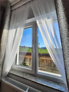 een raam met witte gordijnen en uitzicht bij Casuta bunicilor 