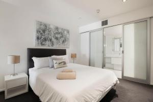 a white bedroom with a large bed with a chair on it at The Sandpiper Sanctuary at Henley Beach in Henley Beach South