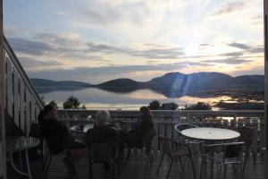 a group of people sitting at tables on a balcony at Ulvsvåg Gjestgiveri og Fjordcamping AS in Ulvsvåg