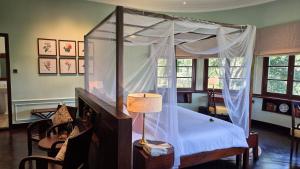 a bedroom with a canopy bed with a lamp and chairs at Ana Mandara Villas Dalat Resort & Spa in Da Lat