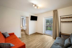 sala de estar con sofá naranja y puerta corredera de cristal en Silbernagl Terrasse - Blick zum See, en Issengo