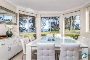 a white dining room with a glass table and white chairs at Aircabin - Tuggerawong - Lake Front - 9 Beds House in Karraganbah