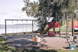 a playground with a slide and swings at Aircabin - Tuggerawong - Lake Front - 9 Beds House in Karraganbah