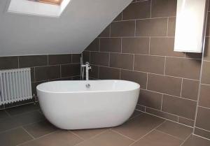 baño con bañera blanca grande y azulejos marrones en Ivy House - Seafront house with garden seating and stunning sea views! - Ocholo Villas, en Filey 8 fotos más