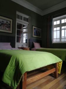 een groene slaapkamer met 2 bedden en 2 ramen bij Posada Casa Real in Huancayo