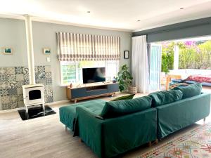 uma sala de estar com um sofá verde e uma televisão em Paradise Beach House with Pool and Parking em Kommetjie