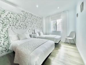 a white bedroom with two beds and a chair at LaFrenchTouch - Céntrico y moderno cerca del tren in Benalmádena