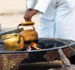 un hombre está agitando una tetera sobre un fuego en Hostel Desert camp Sam, en Jaisalmer