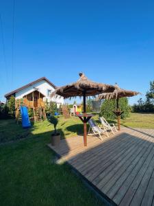 una terrazza in legno con ombrellone, sedie e una casa di Ostrovia - pokoje nad morzem a Ostrowo