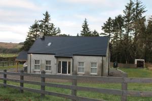 a small house with a black roof in a field at 4 Bedroom Forest View House & Hot Tub Sleeps in Ballynameen