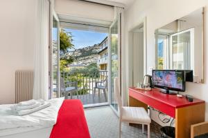 1 dormitorio con cama, escritorio rojo y balcón en Bike & Wind Hotel Villa Maria - Happy Rentals, en Nago-Torbole