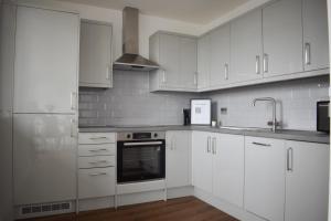 a white kitchen with white cabinets and a sink at Sleek 2 bed with balcony in Brentwood in Brentwood