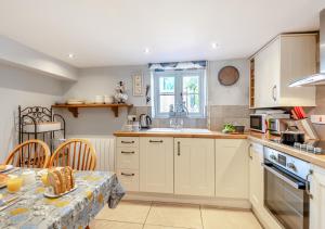 cocina con armarios blancos, mesa y fregadero en White Rose Cottage, en Bodham