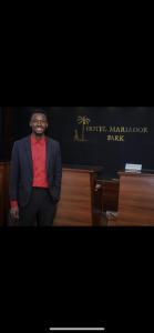 a man in a suit and tie standing in front of a desk at HÔTEL MARIADOR PARK in Conakry