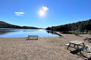 a picnic table and benches on the shore of a lake at Le2085 - Spa et Plage - Les chalets dans le nord in Sainte-Lucie-de-Doncaster