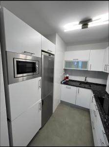 uma cozinha com armários brancos e um frigorífico de aço inoxidável em Primera Linea de Playa Comillas Cantabria em Comillas