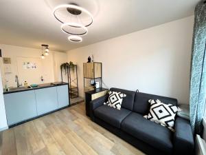 a living room with a black couch and a kitchen at Le Cocon - T2 Neuf avec Parking - Proche Hypercentre & Disneyland in Lagny