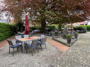 a wooden table with chairs and a red umbrella at Hotel und Restaurant Pinkenburg in Wennigsen
