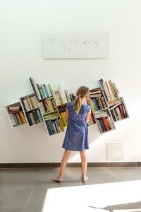 Una mujer con un vestido azul caminando delante de los libros en Wein + Bett Wiedeck, en Stetten