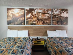 two beds in a hotel room with three paintings on the wall at Days Inn by Wyndham Lafayette Scott in Lafayette