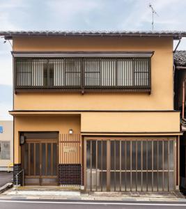 une maison jaune avec un balcon et deux portes de garage dans l'établissement ゲストハウス　luluha, à Awatabe