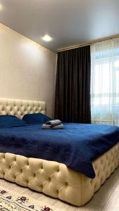 - une chambre dotée d'un grand lit avec des draps bleus et une fenêtre dans l'établissement ЖК Альфа Бета, à Kostanay