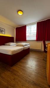 a bedroom with a bed and a window with red curtains at Hotel Gifhorn INN in Gifhorn
