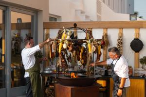 two men are preparing food on a grill at Volcano View by Caldera Collection in Fira +37 photos