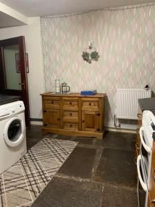 a laundry room with a wooden dresser and a washing machine at Cobblers Cottage in St Margaret's Hope