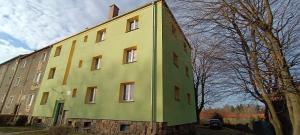 een groen en geel gebouw naast een boom bij Apartament na Poli in Wałbrzych