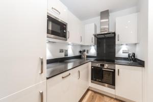 a kitchen with white cabinets and black appliances at Apartments Near The O2 in London