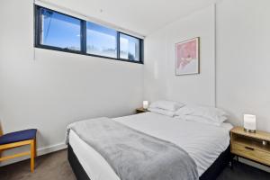 a white bedroom with a bed and a window at Cosy 1-Bed with Private Balcony By Showgrounds in Melbourne