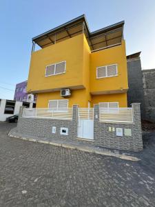 um edifício amarelo com uma cerca em frente em BemVinda Sweet Home - Cama Mesa e Fogão em Praia