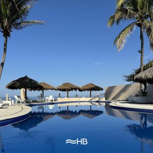 uma piscina com palmeiras e água azul em Hotel Barra de Navidad em Barra de Navidad