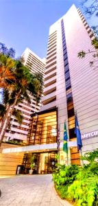 un edificio alto con dos banderas delante en Hotel M-RCURE - Av Paulista - GRAND PLAZA - Deluxe king Studio Veranda - BATH SPA - Executive Class - By LuXXoR en São Paulo