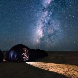 a man laying inside of a tent under the night sky at Abo Yusre Sfari in Bawiti